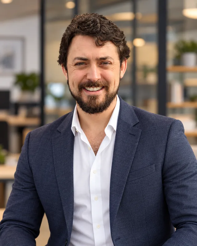 Alex Goldsmith, smiling, in a navy blazer and white open-collared shirt.